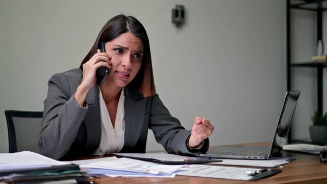 Frustrated office woman talking on the phone while working on her laptop