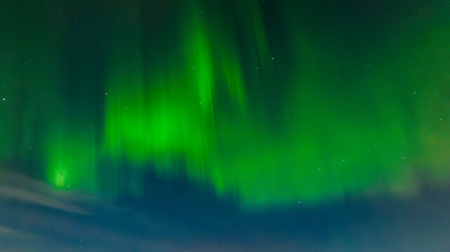 Aerial view of vibrant emerald green aurora borealis dancing across the dark, serene night sky, painting the heavens with ethereal light, Karis, Uusimaa, Finland.