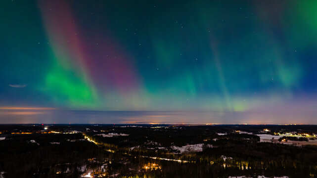 Aerial view of the ethereal aurora borealis painting the night sky with vibrant green and magenta hues over the dark landscape, Karis, Uusimaa, Finland.