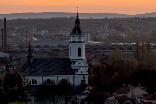  Ostrowiec Świętokrzyski, kolegiata św. Michała Archanioła, stara huta i G&oacute;ry Świętokrzyskie o zachodzie słońca. Kości&oacute;ł z charakterystyczną wieżą zegarową i iglicą stoi na pierwszym planie. 