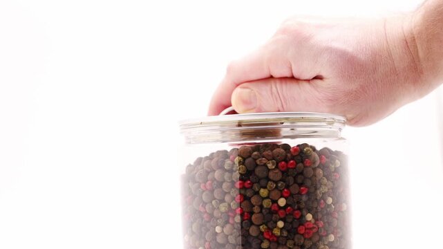 Mixing five types of pepper in a clear jar to create a spice blend