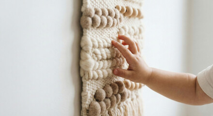Toddler's hand touching textured woven wall hanging macrame for sensory exploration