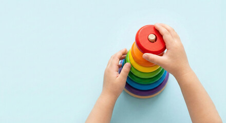 Child's hands stacking colorful wooden rainbow pyramid toy on blue background with copy space