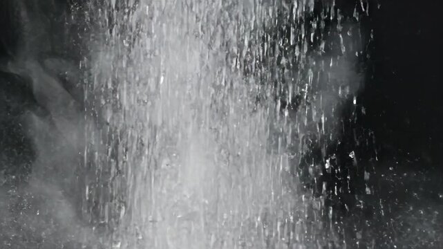 A cascade of white powder falling in slow motion. Fine dust particles exploding like a cloud against a black background. Abstract texture with copy space