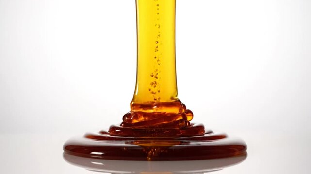 Close up slow motion of amber syrup dripping with bubbles against white background