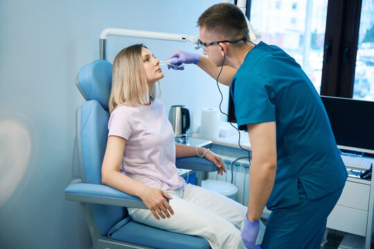 Young male doctor ent, doing nose examination of female patient