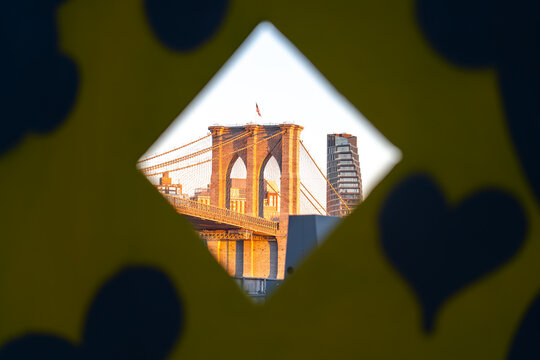 New York, United States - 04 February 2024: View of the golden-hued Brooklyn Bridge, framed by playful, heart-dotted cutouts, with a modern skyscraper rising in the background.