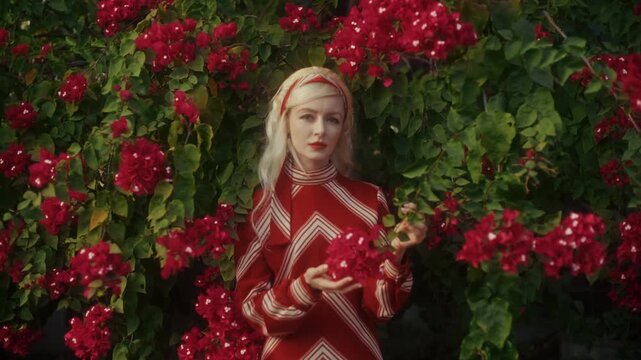 Blonde Woman In Retro Attire By Automobile. Serene Woman Resting Near Vehicle Amidst Lush Flowers