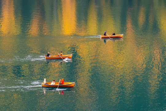 Three wooden rowboats with people on a calm lake reflecting autumn colors. Braies lake,Alto Adige,Dolomites,Italy