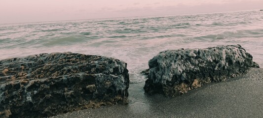 Frozen sea boulders and icy rocks on a sandy beach at sunset. Dramatic winter coast with ocean waves, salt crystals, and arctic textures. High-quality nature photography for commercial use. © Natul'ka