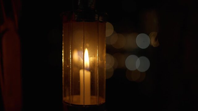 Close up of burning candle inside an antique lantern with beautiful bokeh lights in the background at night.
