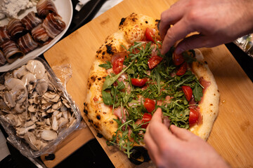 Hands topping fresh homemade pizza with arugula and tomatoes