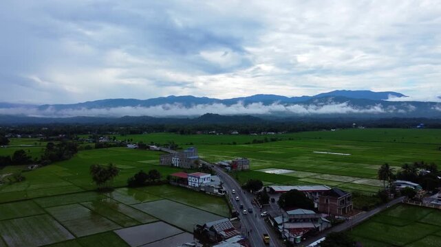 Cinematic aerial footage of a mosque amidst vibrant green sawah and misty mountains, Aceh, Indonesia