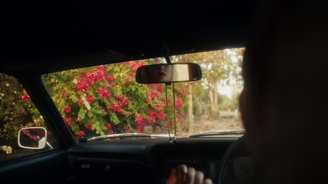 Blonde Woman In Retro Attire By Automobile. Serene Woman Resting Near Vehicle Amidst Lush Flowers