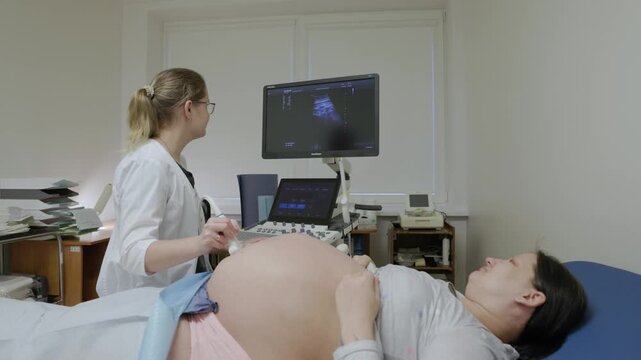 Medical professional performing an ultrasound scan on a pregnant woman, focusing on the abdomen and sonography probe with screen visible in background