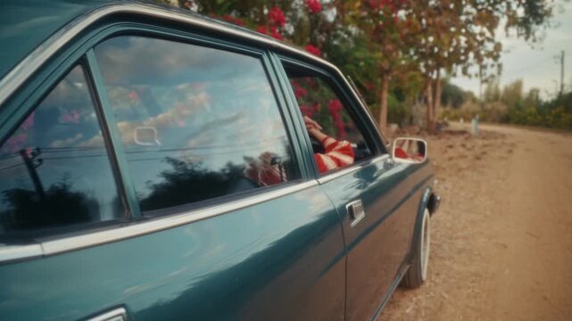 Blonde Woman In Retro Attire By Automobile. Serene Woman Resting Near Vehicle Amidst Lush Flowers