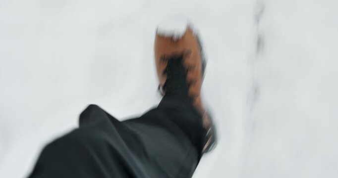 Subjective detail shot following the steady pace of brown leather boots sinking into soft snow.