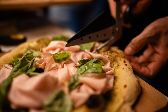 Chef cutting pinsa romana with mortadella basil