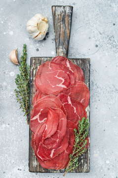 Lean cured beef Cecina arranged neatly with herbs on a wooden board, showcasing vibrant red color over a minimal grey stone background.