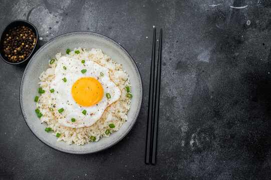 Soft rice and crisp edged fried egg in a rustic bowl photographed on dark textured background for modern culinary content.