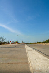 Wide angle shot of a new, empty concrete road extending into the distant horizon under a bright sunny blue sky, conveying travel and future opportunities.