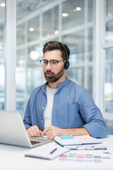 Male professional wearing a headset and spectacles, actively typing on a laptop while working on customer support, telemarketing, or online education in a modern office setup