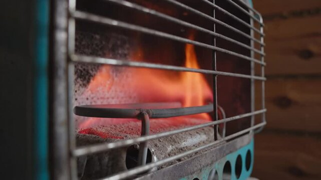 Close up of a propane heater in operation with orange flames and burning fuel viewed behind protective metal grid