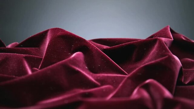 Shifting burgundy velvet cloth settling on gray backdrop under gravity, showing lint and soft light