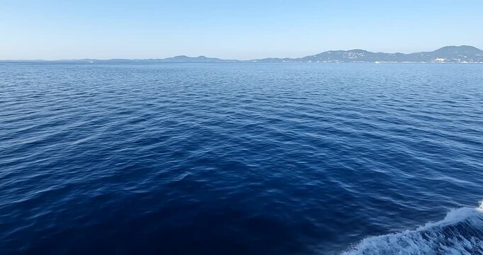 Wide shot from a moving vessel showing the white wake on deep blue Ionian Sea water with hazy mountains on the horizon, perfect for travel and nautical themes.