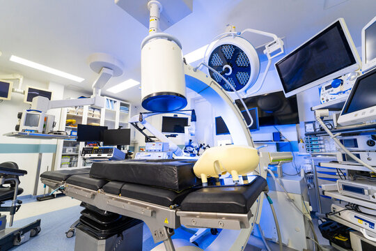 High tech hybrid operating room with robotic x-ray system. Interior of modern surgical suite with C-arm fluoroscopy machine and medical monitors.