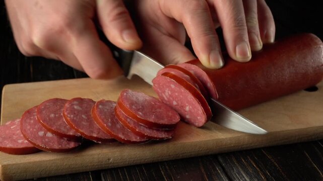 Hands slicing sausage into thin rounds on a wooden cutting board with a sharp knife, showcasing the precision of food preparation in a kitchen setting