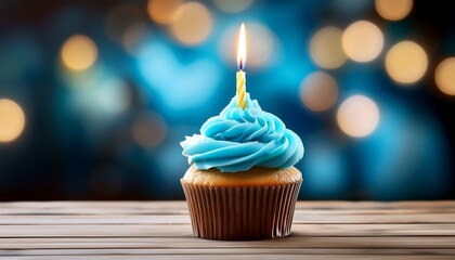 blue frosted cupcake has a lit candle for birthday celebrations on wooden surface against blurry backdrop