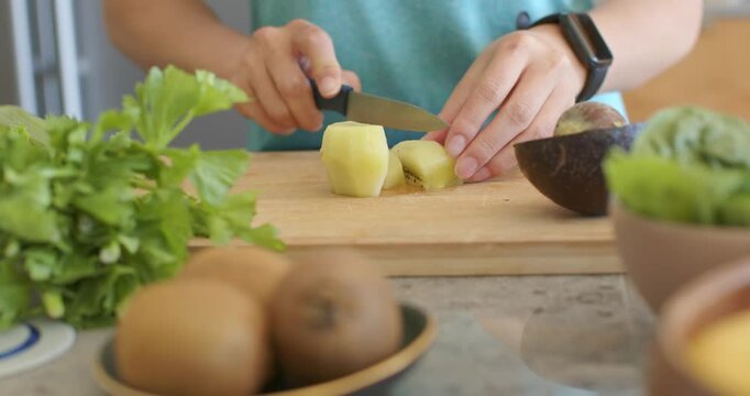 Teal-shirted cook is starting initial cut, slicing peeled potato on board preparing meal