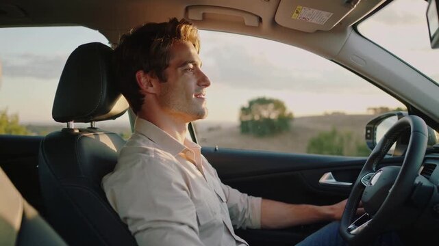 Smiling man driving in light shirt, holding wheel, sunlight through side window easing posture