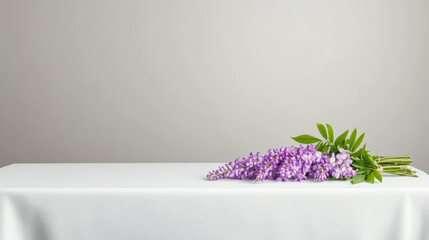 Cascading bouquet of wisteria with green leaves rests on simple white tablecloth, creating serene and elegant atmosphere with soft natural lighting and minimal background