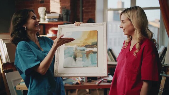 Presenting woman in blue smock rotating abstract painting on reveal in studio, pointing for review