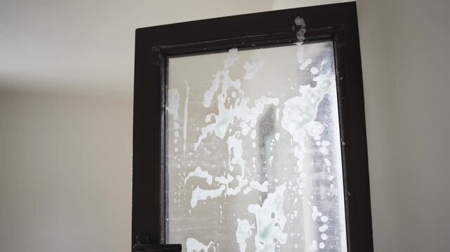 Home hygiene concept with man disinfecting glass windows using spray and gloves during spring cleaning.