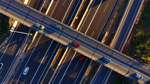 Vehicles move along a highway with several lanes. The scene shows a network of roads and shadows from nearby trees. It is daytime and traffic is flowing smoothly.