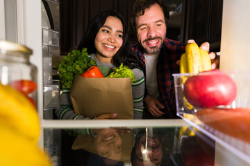 Couple opening fridge, putting groceries, organic food and fresh vegetables for healthy lifestyle