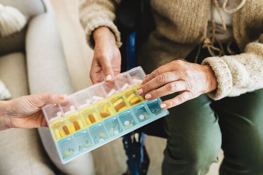 Upper view cropped shot of unrecognizable elderly hands with manicure of disabled female getting colorful pillbox from someone probably in geriatric or retirement home during rehabilitation treatment