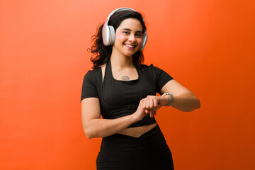 Active woman smiling and checking fitness tracker during studio workout, listening to music with...