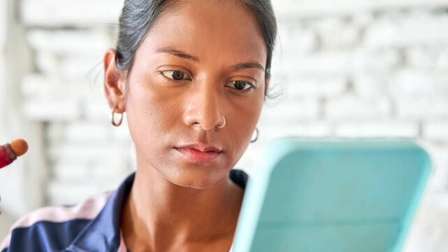 Young latin woman holding a mirror while carefully applying blush to her cheekbones