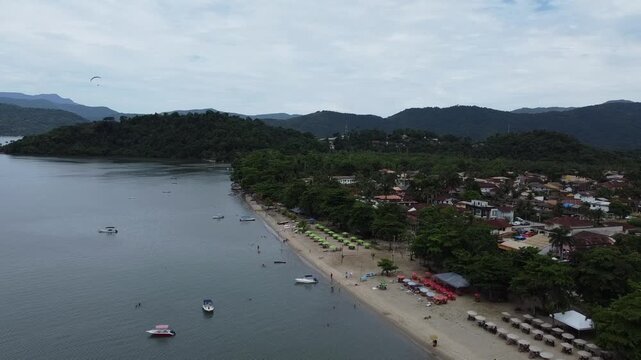 Drone flight along the Jabaquara Beach in Paraty in Brazil. With a stunning view of the coastline, the mountains and the tropical forest, as well as a motorised paraglider in the far distance