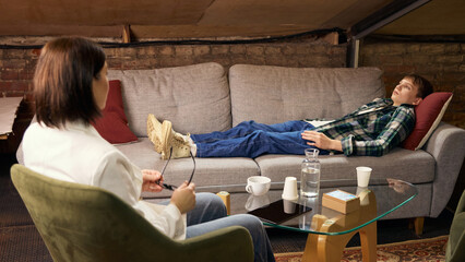 Teenager lying on couch during psychological therapy consultation. Concept of professional mental...