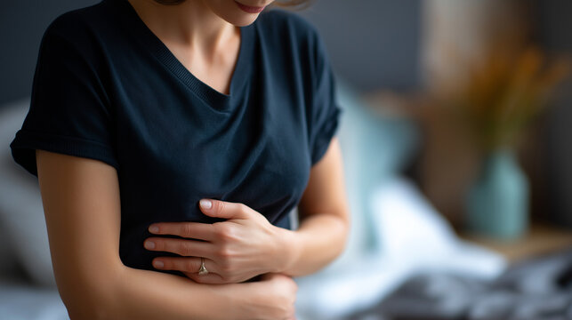 Hand on lower abdomen showing menstrual pain gesture person indicating stomach discomfort from menstruation cramping reproductive health with period pain shown bedroom or home