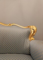 Beautiful luxurious retro sofa with a golden carved armrest and blue silk upholstery, antique furniture
