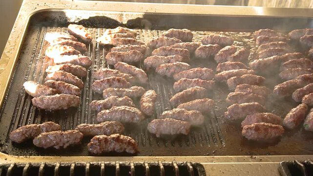 Lula kebab is cooking on a large hot tray in a restaurant kitchen. Turkish kofta. Sizzling Turkish meat patties. Perfect for content about cooking and food preparation. 