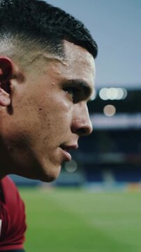 Vertical video: Crouching player tying white or red cleat laces on turf, red kit preparing for match