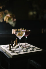 One dirty martini and a twist on espresso martini, standing on a wooden chess board in the dark room, close up view 