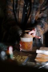 Female bartender standing by the bar counter, making a cocktail, smoking the glass, close up vertical image